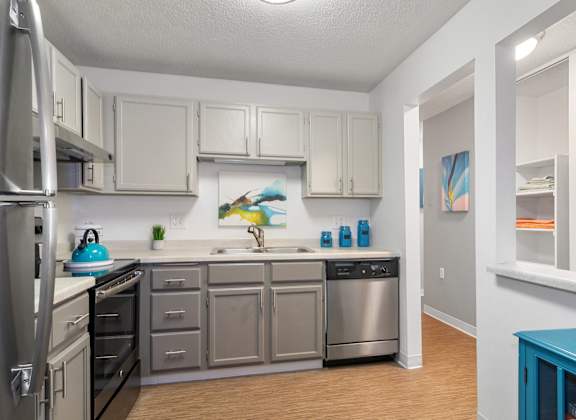 A kitchen with a refrigerator, oven, sink, and cabinets.