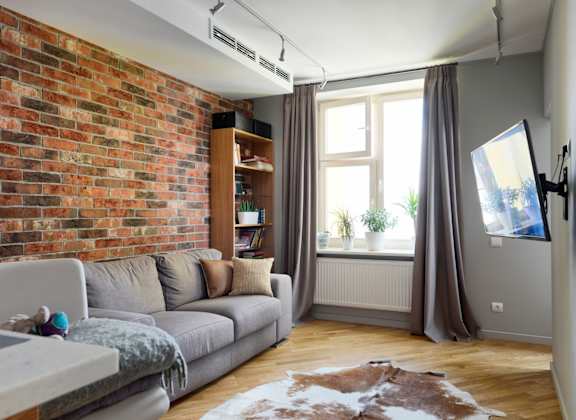 A living room with a grey couch and a brick wall.
