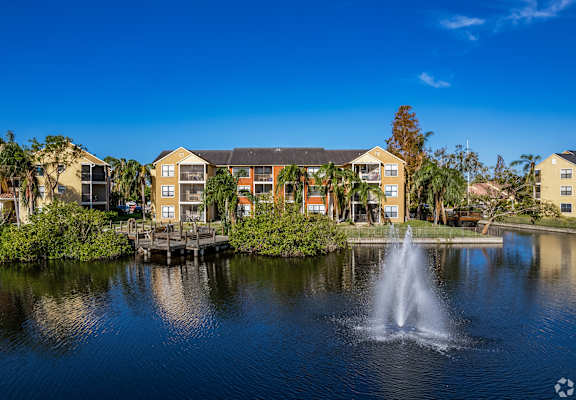 A fountain in the middle of a pond in front of a building.