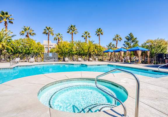 A swimming pool surrounded by palm trees and blue umbrellas.