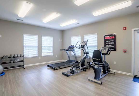 A gym with treadmills, elliptical machines, and a weight rack.