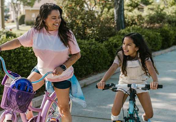 a woman and a girl riding bikes on a sidewalk