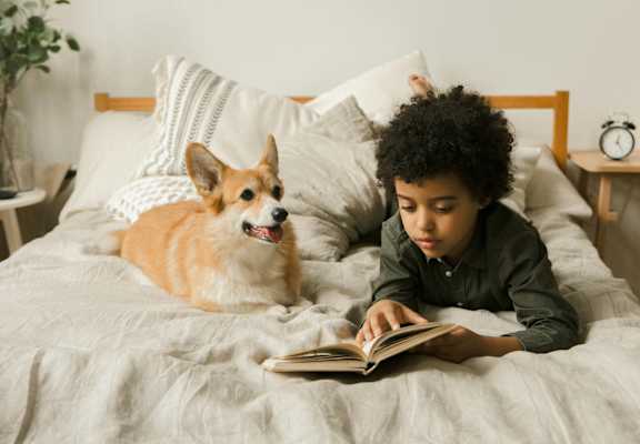 a boy and his dog laying on a bed reading a book
