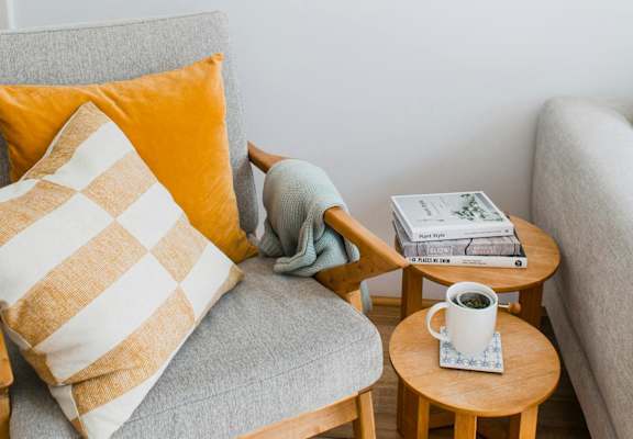 a comfortable chair with pillows and side tables with books and a cup of coffee