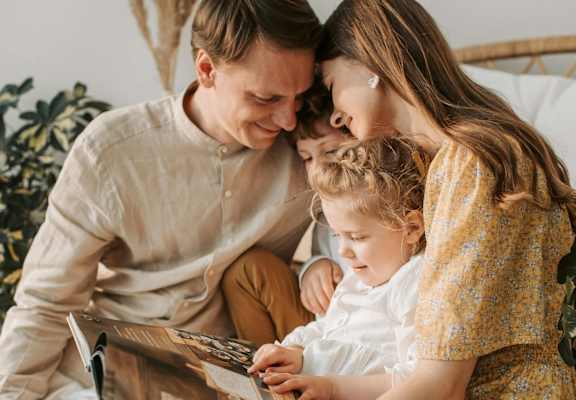 a mother and father reading a book to their daughter and son while sitting on a bed