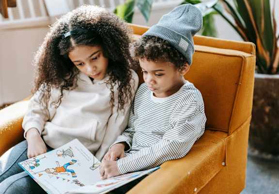 two young children sitting in an orange chair reading a book together