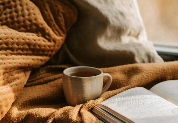 a cup of coffee and an open book on a blanket