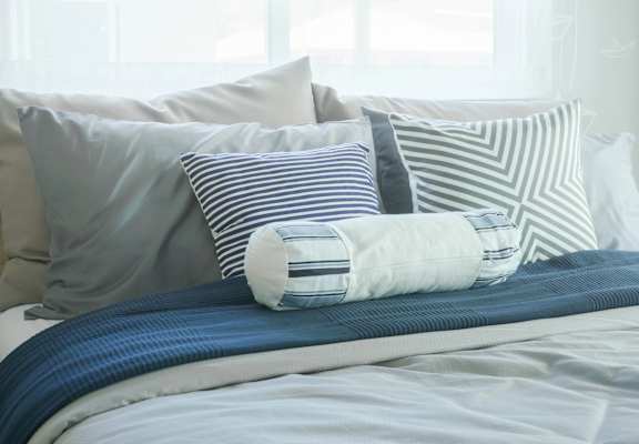 A bed with blue and white pillows and a striped pillow on top.