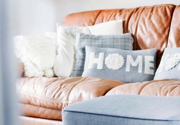 a leather couch with plush pillows. One pillow has the word home on it