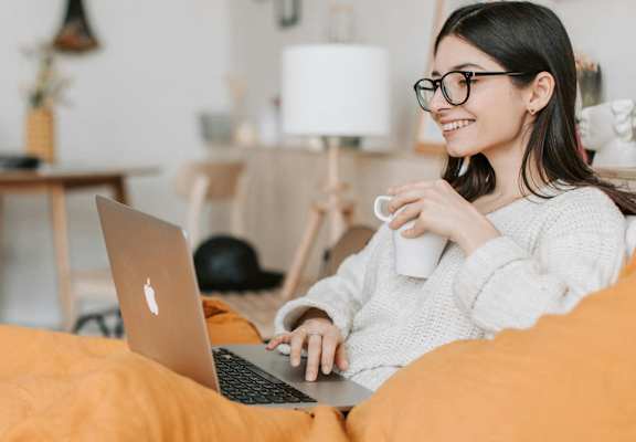 a woman sitting on a bed with a laptop computer and a cup of coffee