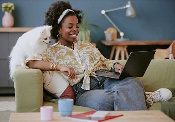 a woman sitting on a couch with a cat on her laptop
