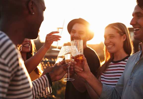 A group of people toasting with glasses of beer at sunset.
