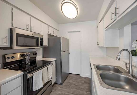 A kitchen with a stove, oven, microwave, refrigerator, and sink.
