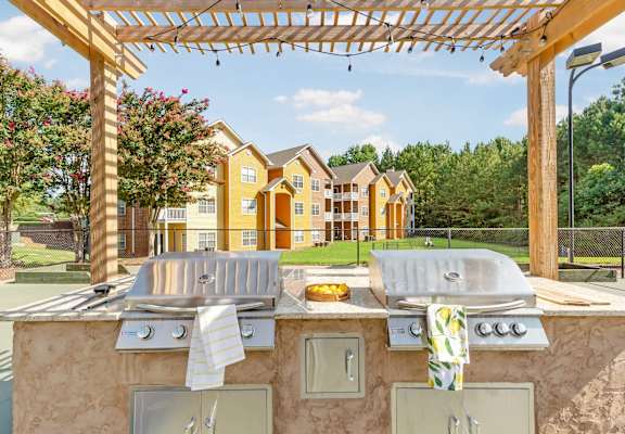 a patio with a grill and two chairs under a pergola