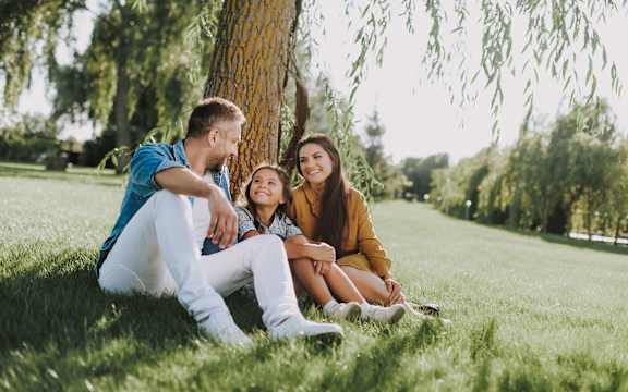 Three people sitting on grass under a tree.