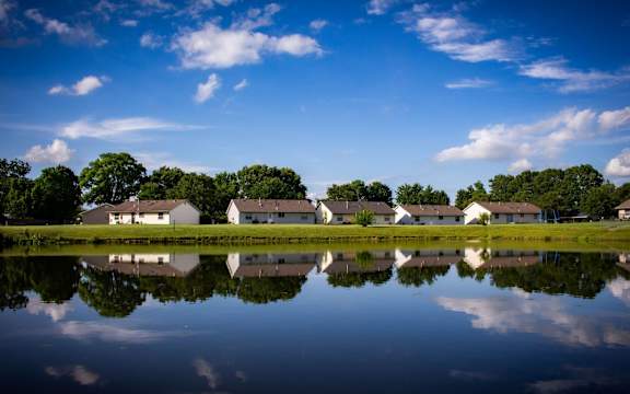 A serene landscape with a row of houses reflected in a calm body of water.