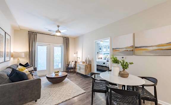 A living room with a grey couch, a round table, and a ceiling fan.