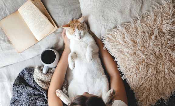 a woman laying on a couch with a cat and a book