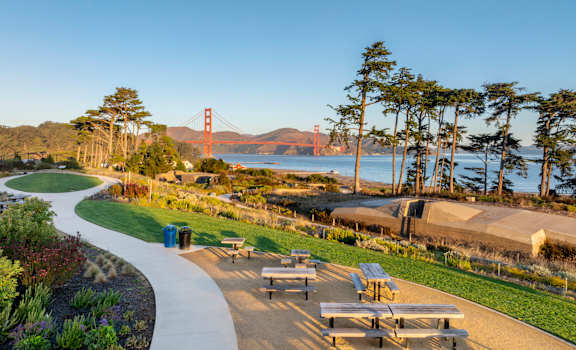 A park with picnic tables and a view of the Golden Gate Bridge.