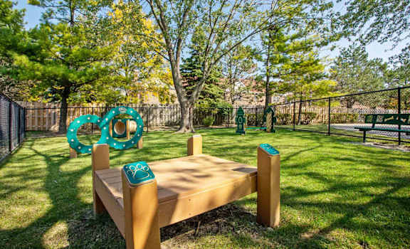 A wooden bench with a green trash can next to it in a park.