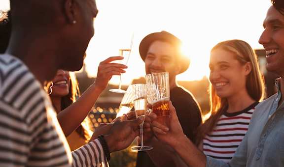 A group of people toasting with glasses of beer at sunset.
