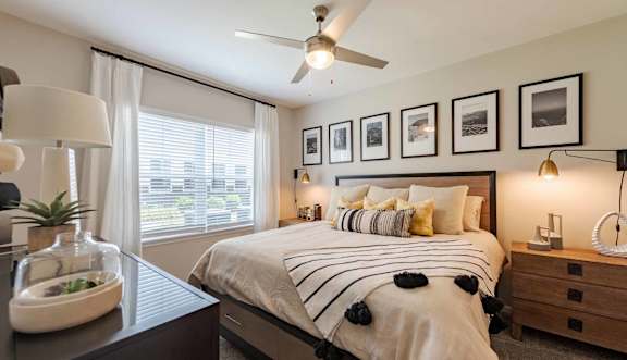 A bedroom with a large bed, a ceiling fan, and framed pictures on the wall.