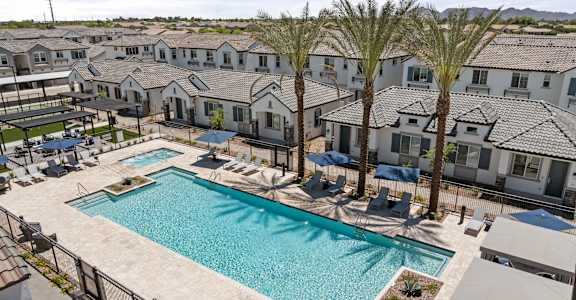 A swimming pool surrounded by palm trees and lounge chairs in a residential area.