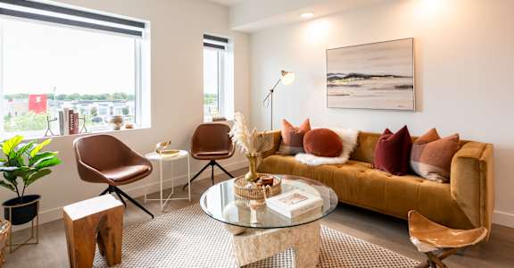 A living room with a brown sofa, a glass table, and a painting on the wall.