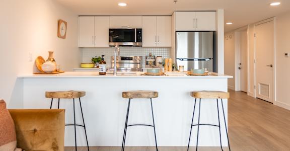 A modern kitchen with white cabinets and a white island with three bar stools.