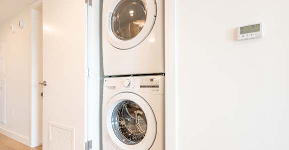 A white washing machine is stacked on top of a white dryer in a laundry room.
