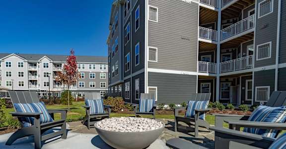 A concrete patio with a bowl of rocks in the middle and chairs around it.
