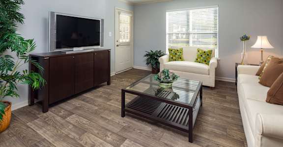 A living room with a white couch, a glass coffee table, and a television.