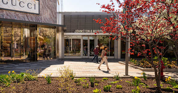 A woman walks past a Gucci store and a Johnston & Murphy store.