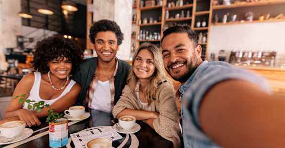 Four people are sitting at a table with cups of coffee in front of them.