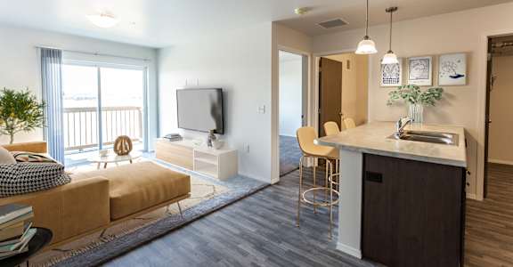 A modern living room with a large window, a sofa, a TV, and a kitchenette.
