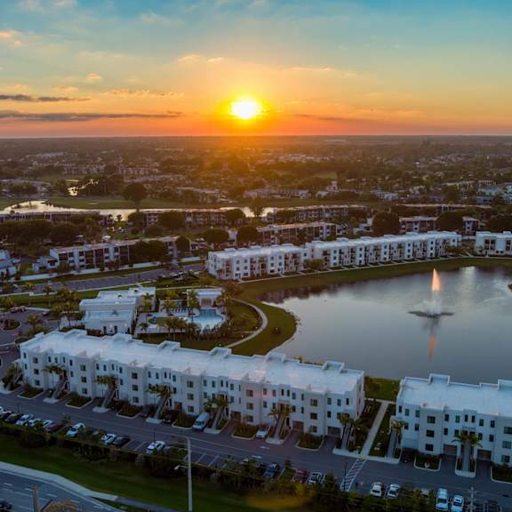 A sunset view of a residential area with a large white building and a fountain in the foreground.