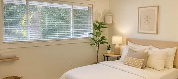 A bedroom with a large bed and a window with blinds.