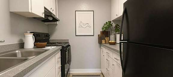A black refrigerator sits in a kitchen with white cabinets and a grey counter.