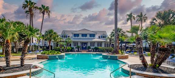 A swimming pool surrounded by palm trees and a building in the background.
