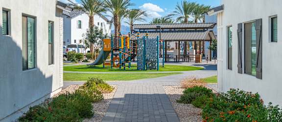 A playground with a slide and swings is surrounded by palm trees.