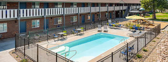 A black fence surrounds a small pool in front of a brick building.