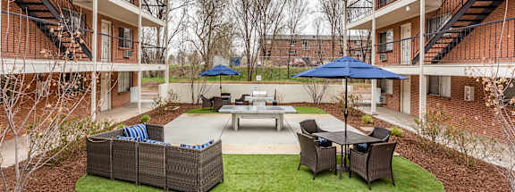 A courtyard with a table, chairs and umbrellas surrounded by buildings.