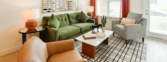 A living room with a green couch, a brown chair, and a black and white plaid area rug