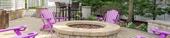 Purple chairs and table around a fire pit in a backyard.