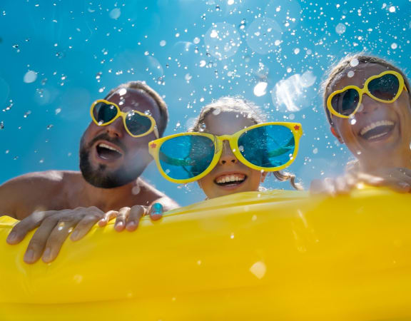 Family of 3 in Yellow Sunglasses Smiling and Hanging Over Edge of Yellow Inflatable Pool Raft 