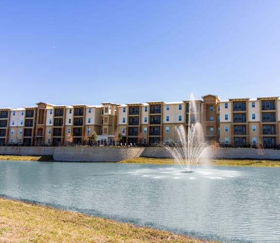 a fountain in the middle of a lake with an apartment building in the background