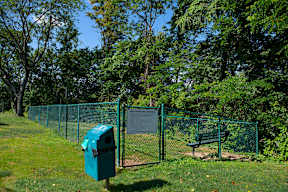 A green trash can sits in front of a chain link fence.