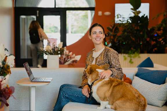 A woman is sitting on a couch with a laptop and a dog.