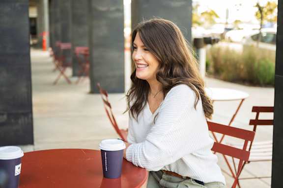 A woman is sitting at a table with a cup of coffee.