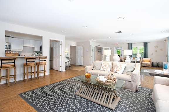 A modern living room with a glass coffee table and a grey rug.